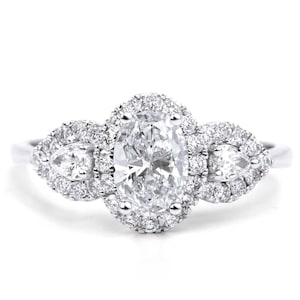May include: A silver ring with a large oval-shaped diamond surrounded by smaller diamonds. Two smaller pear-shaped diamonds are set on either side of the center stone.