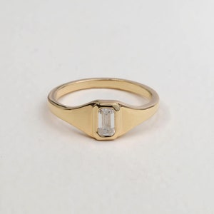 May include: A gold ring with a rectangular, clear gemstone set in a bezel setting.