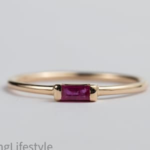 May include: A delicate gold band ring with a single, rectangular ruby gemstone set in the center.