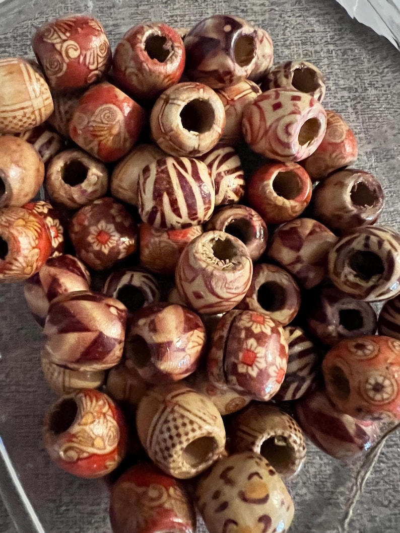 Puede incluir: Una colecci&oacute;n de cuentas de madera con varios patrones y dise&ntilde;os. Las cuentas son marrones, blancas y rojas con detalles intrincados.