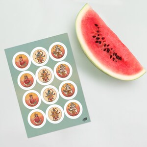 Op de afbeelding: Een vel ronde stickers met kleurrijke illustraties van hindoe&iuml;stische goden, met een plakje watermeloen op een wit oppervlak. De stickers hebben een witte rand en staan op een lichtgroene achtergrond.
