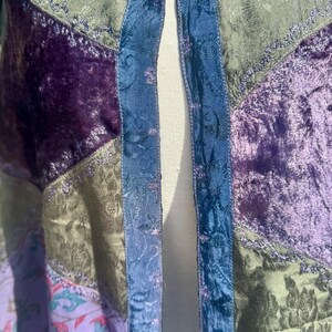 Pode incluir: Um casaco patchwork com tons de roxo, verde e azul. O casaco tem uma textura aveludada e padr&otilde;es florais. As bordas s&atilde;o aparadas com um tecido azul. O casaco &eacute; feito de v&aacute;rios tecidos.