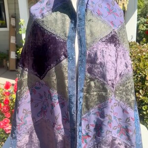 Pode incluir: Um xale de patchwork com uma variedade de tecidos em tons de roxo, verde e azul. O xale apresenta padr&otilde;es florais, veludo e uma borda com franjas. O design inclui um painel central e patches em forma de diamante.