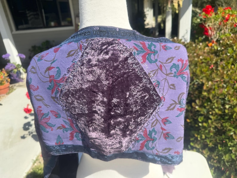 Pode incluir: Bolero roxo com um painel central de veludo e mangas estampadas com flores. As mangas s&atilde;o de um roxo mais claro com desenhos florais vermelhos, verdes e azuis. O casaco tem uma borda azul escura e texto ao longo da gola.