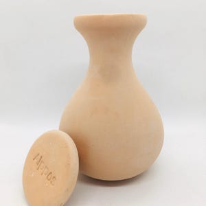 Op de afbeelding: Een lichtbruine terracotta vaas met een afgeronde body en uitlopende hals, naast een kleine, ovaalvormige steen. De steen heeft het woord "Appos" in het oppervlak gegraveerd. De vaas en steen staan tegen een witte achtergrond.