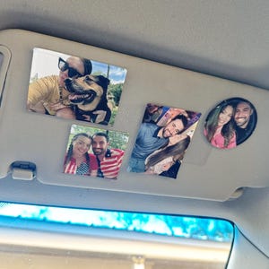 May include: Four photos are displayed on a car's sun visor. The photos are of couples and a woman with a dog. The photos are printed on a white background and are surrounded by a black border.