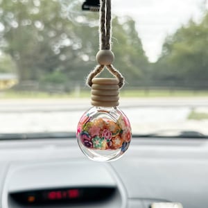 May include: A clear glass car air freshener with a wooden top and a string for hanging. The glass is filled with colorful flower-shaped beads.