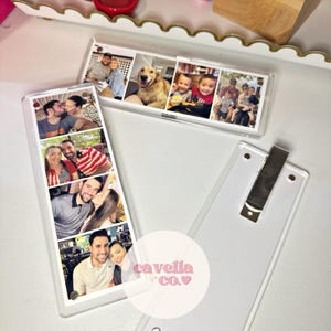 May include: Clear acrylic photo holders with multiple family photos. One holder is upright, and the other is horizontal. The photos show couples, children, and a dog. The brand name "cavella co." is visible.