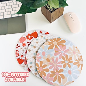 May include: Three round mouse mats with different retro floral patterns. The mouse mats are stacked on top of each other. The top mouse mat has a light blue, pink, and brown floral pattern. The middle mouse mat has a white and blue geometric pattern. The bottom mouse mat has a red, pink, and white floral pattern. The text "100+ PATTERNS AVAILABLE!" is written below the mouse mats.