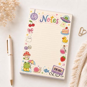 May include: A rectangular notepad with cream-colored lined paper featuring the word Notes in colorful letters at the top. The border is decorated with small illustrations including a disco ball, cherries, a bow, a ghost, dice, a mushroom, a frog with an umbrella, a snail, a fish, a cassette tape, a strawberry, a potion bottle, a rubber duck, a slice of cake, and a frog in a UFO.