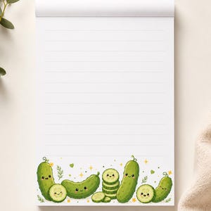 Può includere: Un blocco note bianco con linee orizzontali caratterizzato da un'illustrazione sul bordo inferiore di vari cetrioli verdi in stile cartoon con facce sorridenti, alcuni tagliati a fette, accentuati da piccole stelle gialle, rametti verdi e minuscoli cuori.