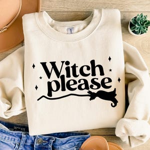 Op de afbeelding: Crèmekleurige sweatshirt met de zwarte tekst "Witch please", vergezeld van een afbeelding van een bezem. Het ontwerp bevat kleine ster- en diamantaccenten, perfect voor Halloween of evenementen met een heksenthema.