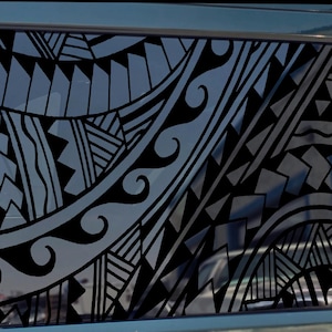 May include: Black tribal pattern window decal applied to a vehicle window. The design features a complex arrangement of geometric shapes, lines, and curves. The decal is applied to a rectangular window.