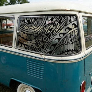 May include: A vintage teal and white Volkswagen van with a decorative black and silver window design. The van has a classic design with a white roof and chrome accents. The window design features geometric and wave-like patterns.