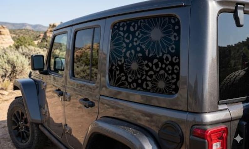 May include: A dark gray SUV features a rear side window decorated with a black decal. The decal displays a repeating pattern of large daisy flowers layered over a leopard print background, covering the entire surface of the glass window.