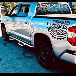 May include: A silver pickup truck featuring black tribal-style decals on the rear quarter panel and the rear window. The text TRD 4X4 OFF ROAD is printed in red and black on the side. The vehicle has black wheels and chrome side steps.