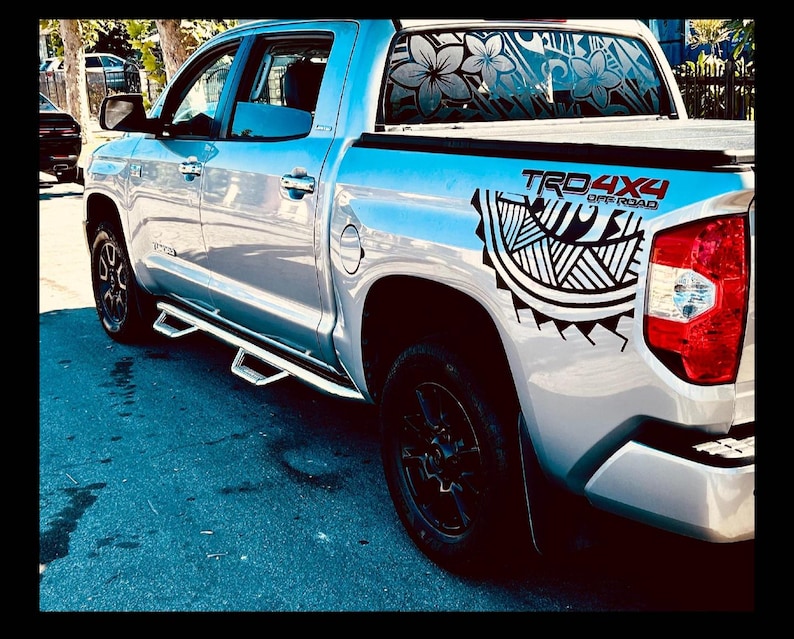 May include: A silver pickup truck featuring black tribal-style decals on the rear quarter panel and the rear window. The text TRD 4X4 OFF ROAD is printed in red and black on the side. The vehicle has black wheels and chrome side steps.