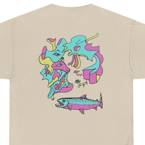 May include: A beige t-shirt featuring a graphic print on the back. The design includes abstract, flowing shapes in bright turquoise and pink, alongside a detailed illustration of a fish colored in turquoise and pink with a black outline.