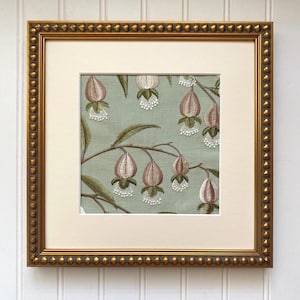 May include: Framed artwork featuring an embroidered floral design. The artwork showcases a light green background with detailed embroidery of pink and white flowers and green leaves. The frame is gold with a beaded edge.
