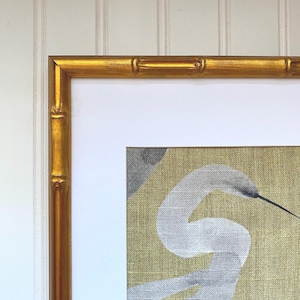 May include: A framed artwork featuring a white heron against a gold and gray background. The frame is a bamboo-style design with a gold finish. The artwork is mounted on a white mat.