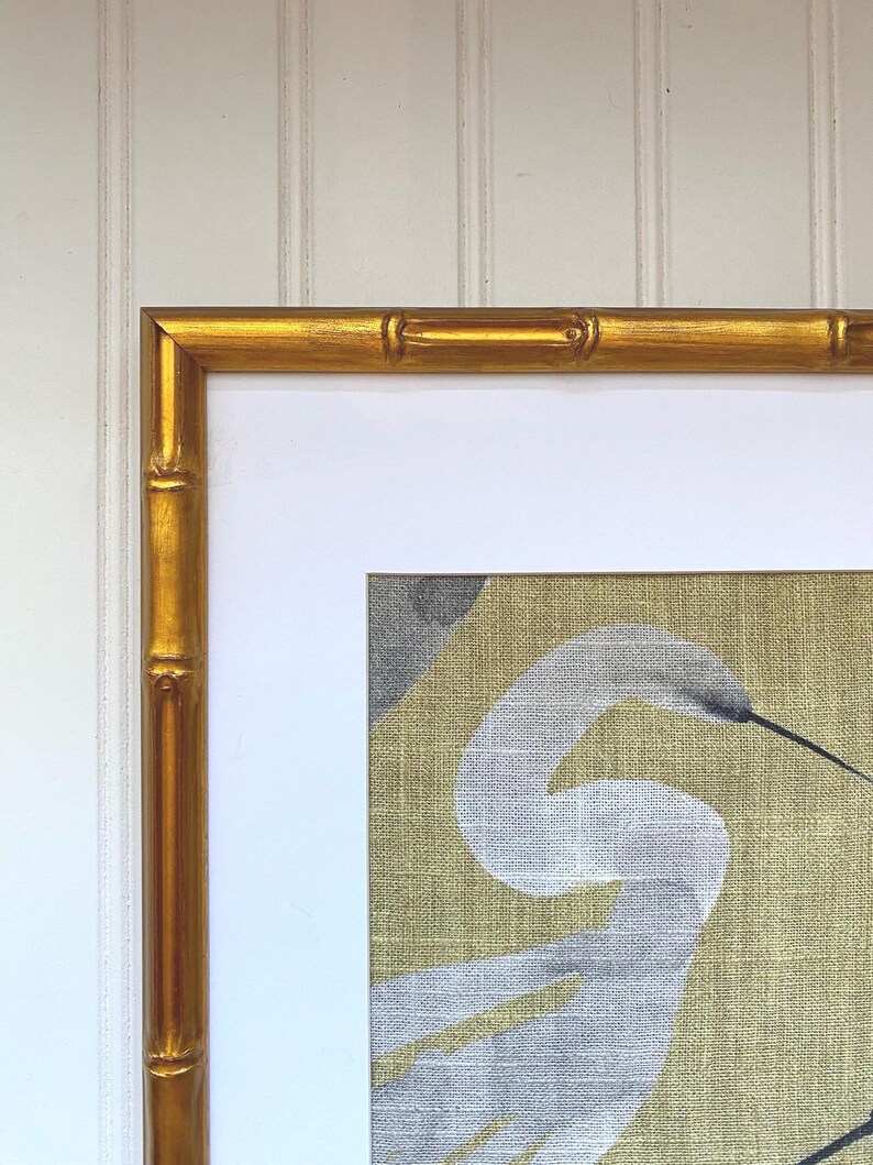 May include: A framed artwork featuring a white heron against a gold and gray background. The frame is a bamboo-style design with a gold finish. The artwork is mounted on a white mat.