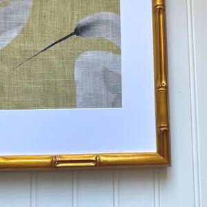 May include: A framed artwork featuring a botanical print with white and gray floral elements against a yellow-green background. The frame is a gold bamboo style, adding a touch of natural elegance to the piece.
