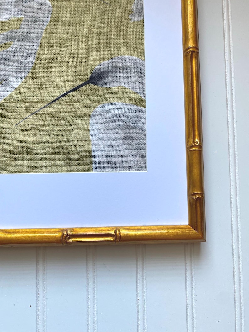 May include: A framed artwork featuring a botanical print with white and gray floral elements against a yellow-green background. The frame is a gold bamboo style, adding a touch of natural elegance to the piece.
