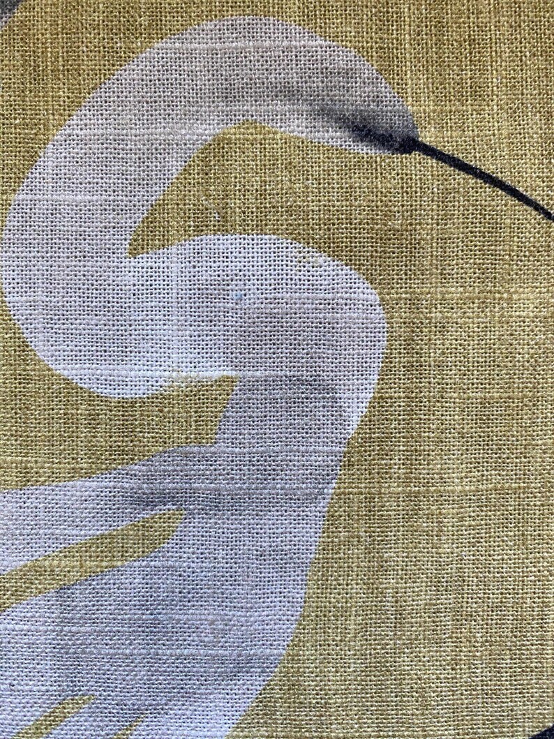 May include: Close-up of a fabric with a white bird design on a golden-yellow background. The bird's body is white, with a gray head and a long black beak. The fabric has a textured appearance.