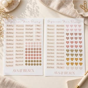 Peut inclure: Deux feuilles d'autocollants blanches intitulées Organise Your Diary avec la marque AVA & BEAUX. Les feuilles présentent diverses étiquettes rectangulaires avec du texte comme Birthday, Vacation et Next Month, ainsi que des rangées d'autocollants ronds et en forme de cœur.