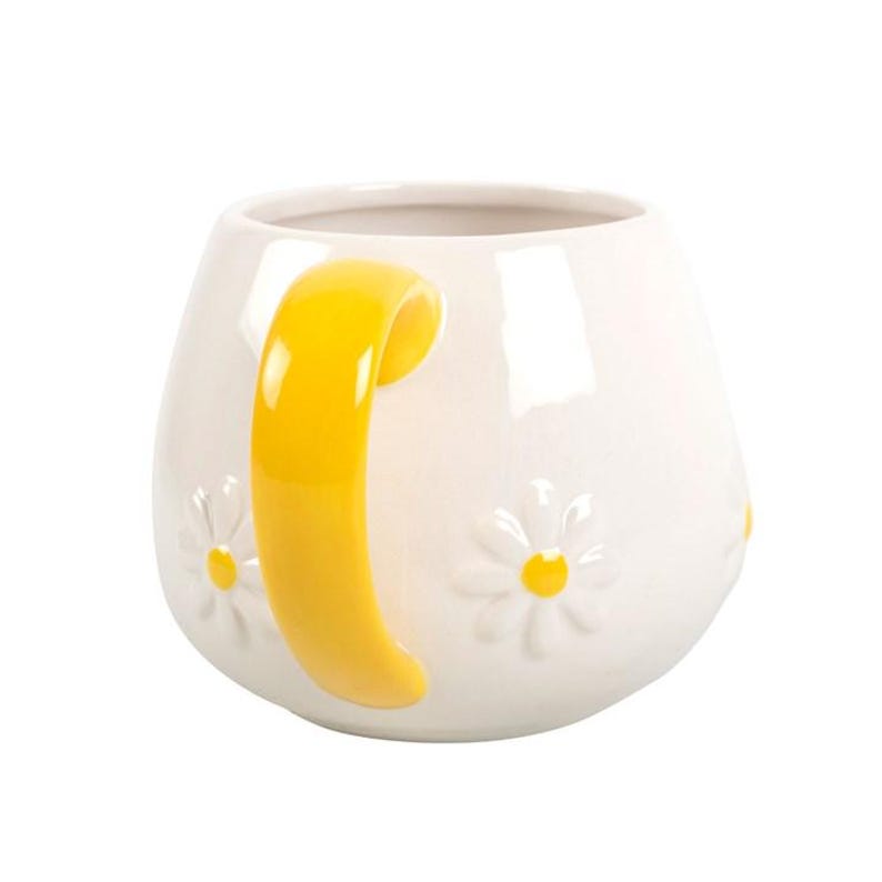May include: White ceramic mug with a yellow handle and embossed daisy flowers. The mug has a rounded shape and a glossy finish. The daisies have yellow centers. A charming and cheerful design for a coffee or tea cup.