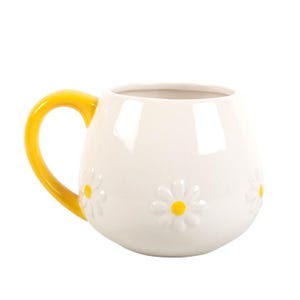 May include: White ceramic mug with a yellow handle. The mug features embossed daisy flowers with yellow centers. The mug is a rounded shape, perfect for coffee or tea.