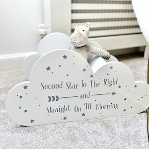 Op de afbeelding: Een wit, wolkvormig rek met grijze sterren en de tekst "Second Star To The Right and Straight On 'Til Morning". Een knuffelneushoorn zit op het rek.