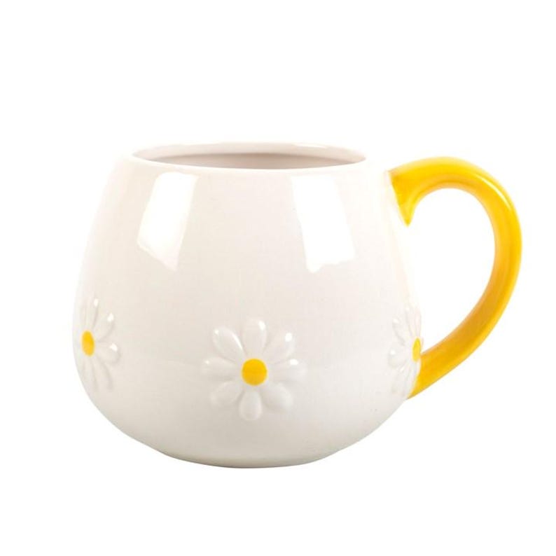 May include: White ceramic mug with a yellow handle. The mug features embossed daisy flowers with yellow centers. The mug has a rounded shape and is suitable for hot or cold beverages.