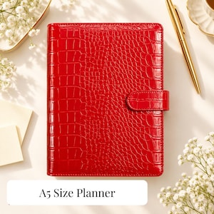 Op de afbeelding: Een felrode A5-planner met een glanzende krokodillenleertextuur en een bijpassende zijsluiting. De rechthoekige planner is voorzien van een duidelijk reliëfpatroon over de gehele voorzijde, wat zorgt voor een glanzende afwerking.
