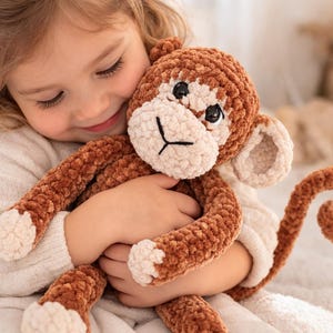 Puede incluir: Un mono de peluche hecho de hilo suave de color marrón y crema. El juguete de peluche presenta una cara redonda con ojos de plástico negro, una boca bordada, orejas grandes y una cola larga y rizada. Las manos y los pies son de color crema.