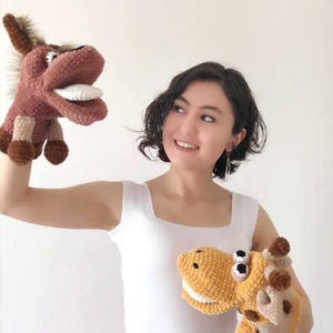 May include: Handmade crochet puppets of a donkey and a giraffe. The donkey puppet is brown and tan, while the giraffe puppet is yellow, brown, and white. The puppets have detailed features, including eyes, mouths, and hooves. The puppets are designed for children's play.