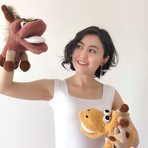 Può includere: Due marionette di animali fatte a mano all'uncinetto: un asino marrone con la lingua bianca e una giraffa gialla con occhi neri e bianchi. Le marionette sono fatte di filato morbido e hanno dettagli.