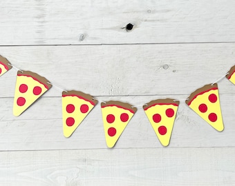 May include: A string of pizza slice-shaped paper pennants with red pepperoni on a yellow background. The pennants are strung together with white string and are hanging against a white wood background.