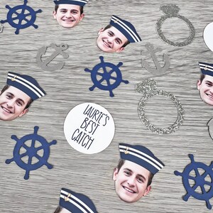 May include: A collection of confetti featuring a man's face wearing a sailor hat, anchors, steering wheels, and rings. The confetti also includes two white circles with the text "Laurie's Best Catch".