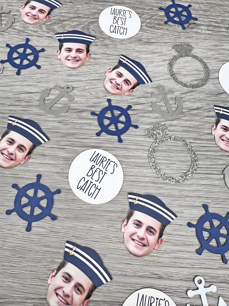 May include: A collection of confetti featuring a man's face wearing a sailor hat, anchors, steering wheels, and rings. The confetti also includes two white circles with the text "Laurie's Best Catch".