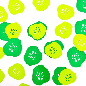 May include: A collection of green and yellow paper cutouts in the shape of cucumbers. The cutouts have a lacy design and are scattered on a white background.