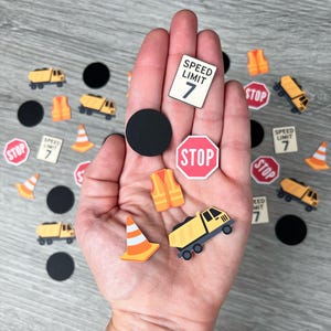 May include: A collection of miniature construction-themed cutouts, including a yellow dump truck, orange safety cones, and stop signs. The image also features speed limit signs with the number 7 and black circles.