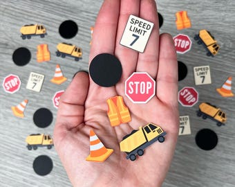 May include: A collection of miniature construction-themed cutouts, including a yellow dump truck, orange safety cones, and stop signs. The image also features speed limit signs with the number 7 and black circles.