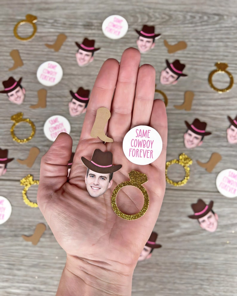 K&ouml;nnte beinhalten: Eine Hand h&auml;lt eine Vielzahl von Konfetti f&uuml;r eine Hochzeit oder eine Party. Das Konfetti umfasst Cowboyh&uuml;te, Stiefel, Ringe und Kreise mit dem Text "Same Cowboy Forever".