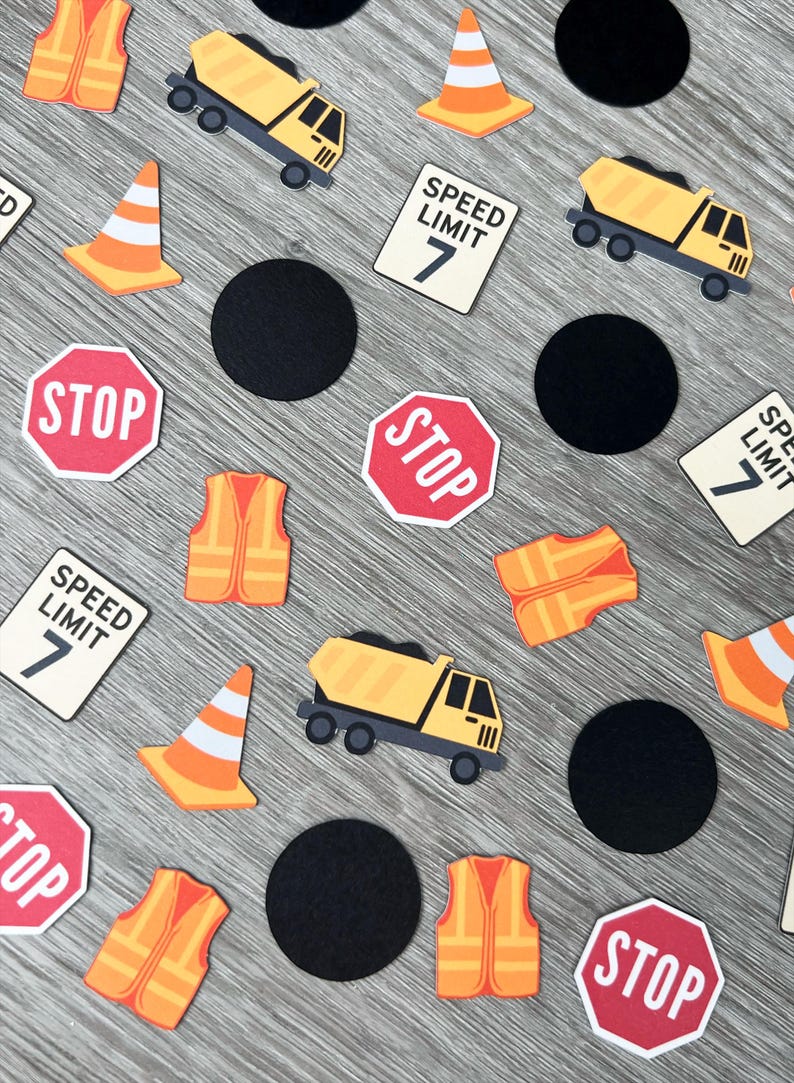 May include: Construction-themed confetti featuring yellow dump trucks, orange safety vests, traffic cones, black circles, and stop signs with the text "STOP". Also included are signs with the text "SPEED LIMIT 7".