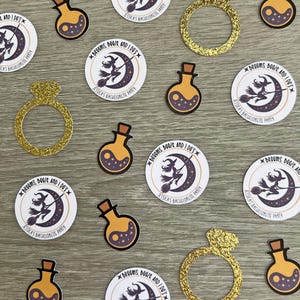 May include: An assortment of party decorations, including gold glitter engagement rings and potion-shaped bottles with a yin-yang design. Round stickers feature a witch on a broom and the text "Brooms, Booze and I Do's" for a bachelorette party.
