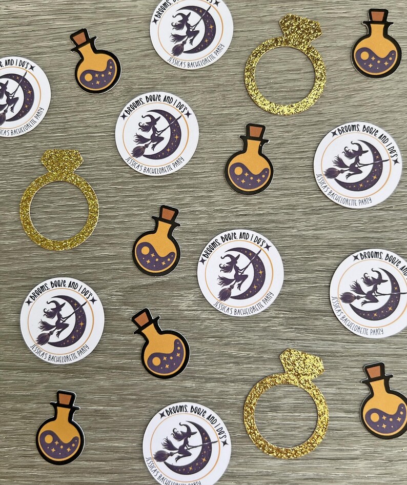 May include: An assortment of party decorations, including gold glitter engagement rings and potion-shaped bottles with a yin-yang design. Round stickers feature a witch on a broom and the text "Brooms, Booze and I Do's" for a bachelorette party.