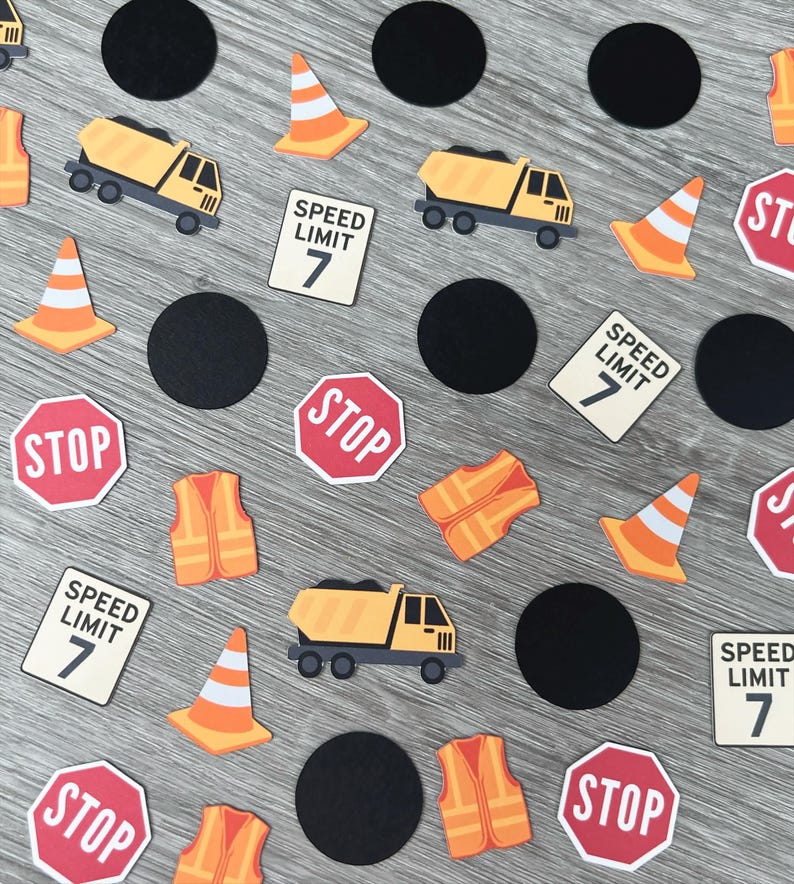 May include: Construction-themed confetti featuring yellow dump trucks, orange traffic cones, stop signs, speed limit signs, black circles, and orange safety vests. The speed limit signs read "SPEED LIMIT 7".