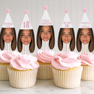 May include: Five cupcakes with pink frosting, each topped with a personalized face cutout wearing a white party hat. The hats feature pink text reading Birthday Girl, 18, Hello EIGHTEEN, THE BIG 18, and EIGHTEEN & THRIVING, all topped with a small pink pom-pom.