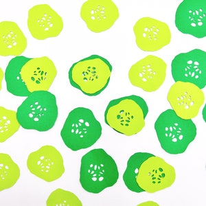 May include: Green and yellow paper cutouts of cucumber slices. The cutouts are scattered on a white background.